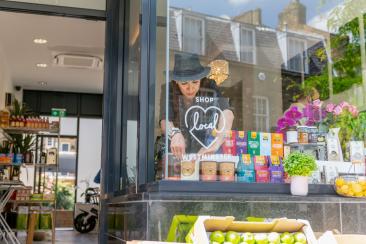 Woman adding a sign that reads 'shop local, Westminster' to the window of her shop